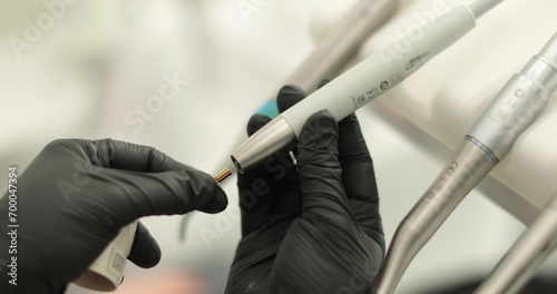 The hands of a female dentist are holding a drill in their hands. Close-up of a dental drill in the hands of a doctor wearing black gloves.