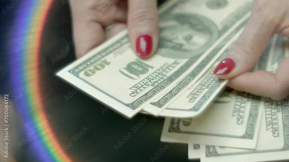 Female hands counting a wad of money - 100, 50 dollar bills. Closeup. Macro. A rainbow flare from a spot light decorates the frame