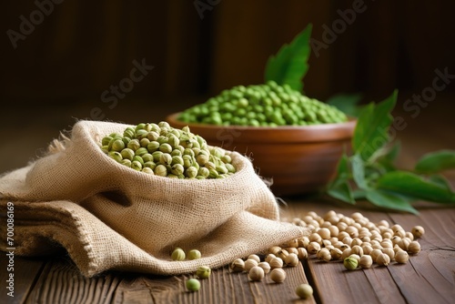 Heap of uncooked dried chickpeas in a burlap sack alongside raw green chickpea pods and a plant on a wooden table photo