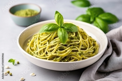 Pesto spaghetti with fresh basil in a gray bowl on a light gray background.