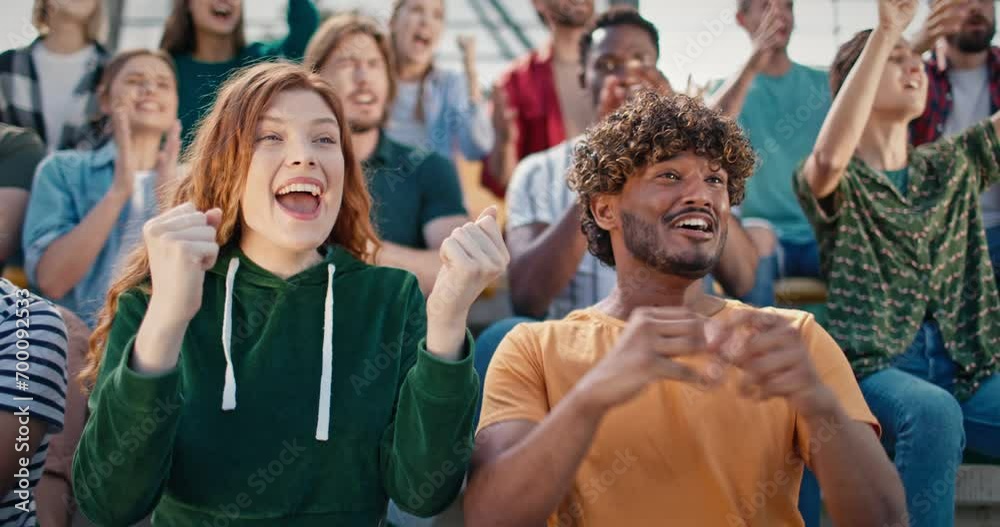 Happy woman watching soccer match with her multi-ethnic friend in arena full of fans. People celebrating scoring goal against their opponent. Happy crowd congratulating their team on victory.