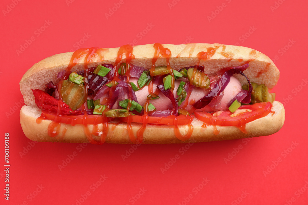 Tasty hot dog with onion, tomato, pickles and sauce on red background, top view Tasty hot dog with onion, tomato, pickles and sauce on red background, top view