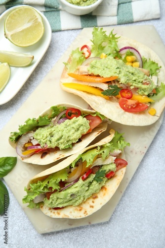 Delicious tacos with guacamole, meat and vegetables on light grey table, flat lay