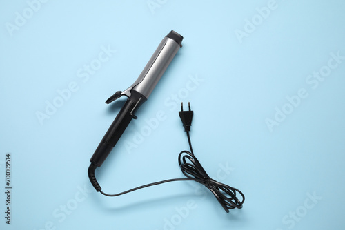 One curling iron on light blue background, top view. Hair styling appliance