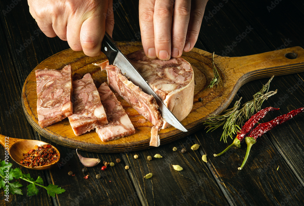 Slicing headcheese on a kitchen board before setting the table in a restaurant for lunch. Knife in the hand of a cook while cutting brawn