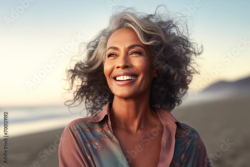 Smiling mature woman at the beach, happy, natural, relaxed and free lifestyle, enjoying sunny and windy weather, breathing ocean air photo