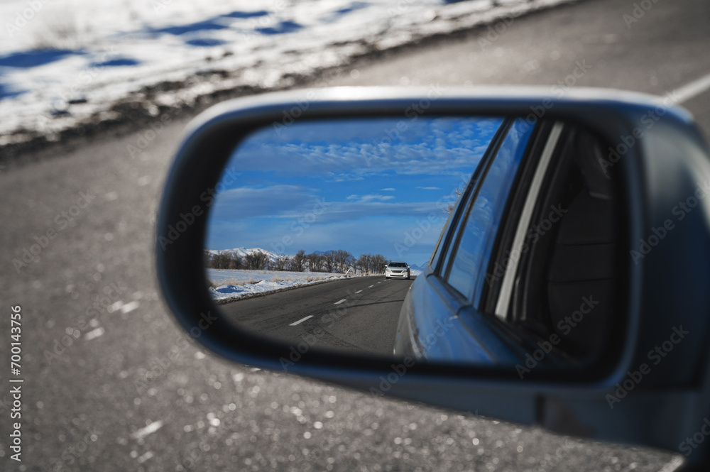 reflection of a beautiful winter landscape with a road and mountains in the snow in rearview mirror of the car. The concept of festive holiday winter travel
