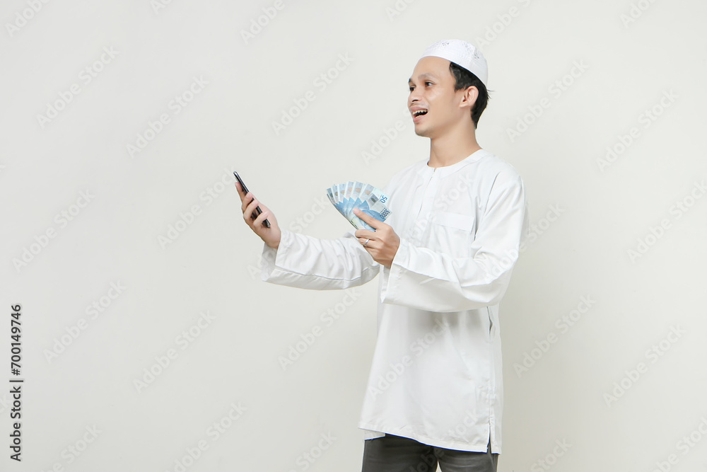 happy muslim man holding money rupiah banknotes and  mobile phone. People religious Islam lifestyle concept. celebration Ramadan and ied Mubarak. on isolated background.
