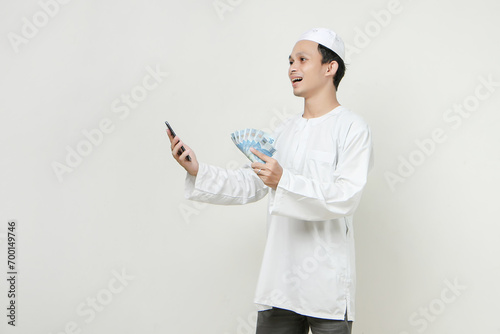 happy muslim man holding money rupiah banknotes and mobile phone. People religious Islam lifestyle concept. celebration Ramadan and ied Mubarak. on isolated background.