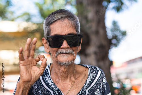 A cool hippie granddad saying its ok. Wearing shades and boho style shirt. Hanging out at the park. photo