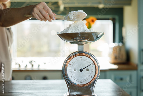 Woman's hand putting flour on an antique scale on the kitchen counter