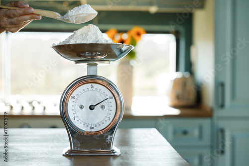 Woman's hand putting flour on an antique scale on the kitchen counter photo