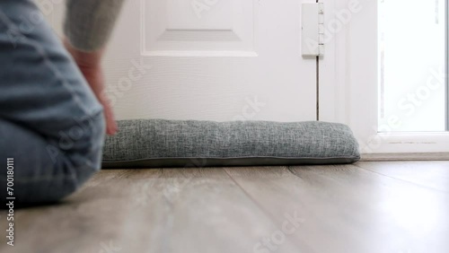 Close Up Of Man Saving Energy Insulating Home Putting Draught Excluder Against Front Door