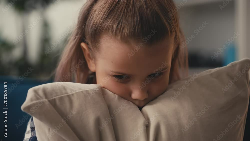Little girl feeling upset while sitting on couch, hugging a pillow for comfort