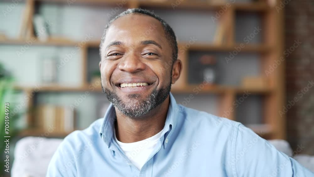 Portrait of happy mature African American male in shirt sitting on sofa in living room at home office. Head shot of a positive businessman. A smiling freelancer poses looking at the camera. Close up Portrait of happy mature African American male in shirt sitting on sofa in living room at home office. Head shot of a positive businessman. A smiling freelancer poses looking at the camera. Close up