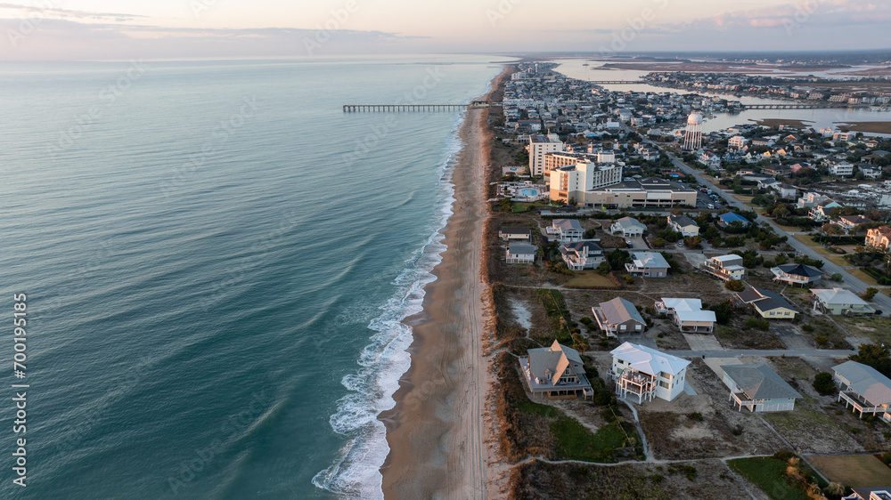 Aerial dawn view of Wrightsville Beach with a pier extending into the calm sea and coastal homes lining the shore.