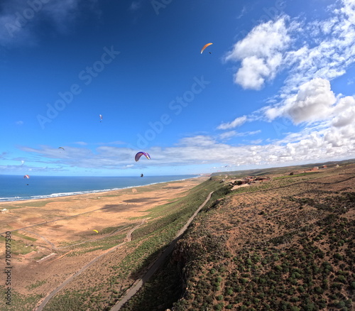 beauty of paragliding flying over scenic seaside landscape,sand dunes and mountain terrain,aerial apnorama landscape view,paragliding pilot with his paraglider wing,aerial extreme sports,action camera photo