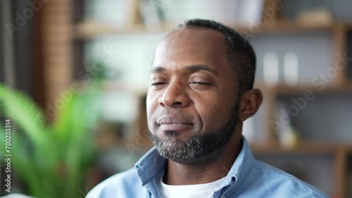 Close up of a mature african american man relaxing with his eyes closed while sitting on sofa in living room at home. Face of calm happy senior bearded male resting after work and looking at camera photo