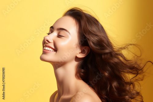 portrait of a happy young woman of model appearance in profile with long luxurious hair on a bright yellow background. The sphere of beauty and fashion