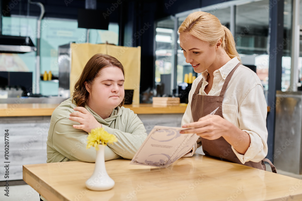 smiling waitress showing menu card to thoughtful woman with down syndrome sitting at table in cafe