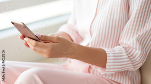 close-up of a woman's hands holding a smartphone, with one hand adorned with a ring, set against her striped shirt and pink skirt.
