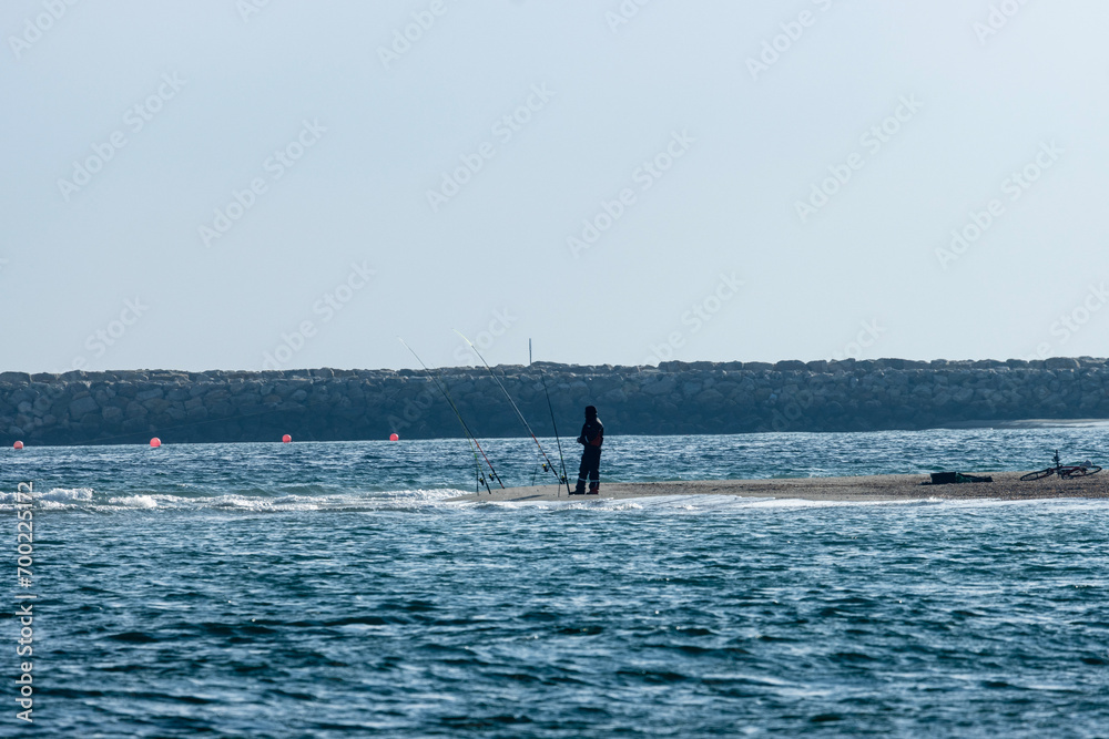 Obraz premium A lone fisherman stands at the seashore, casting his line into the rhythmic dance of the waves. The rhythmic sound of waves crashing on the shore provides a soothing backdrop to his patient endeavors.