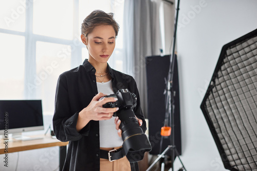 young attractive female photographer in casual outfit looking at photos on her camera in studio