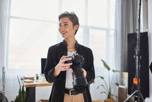 merry female photographer in casual clothes with camera in her hands smiling and looking away photo