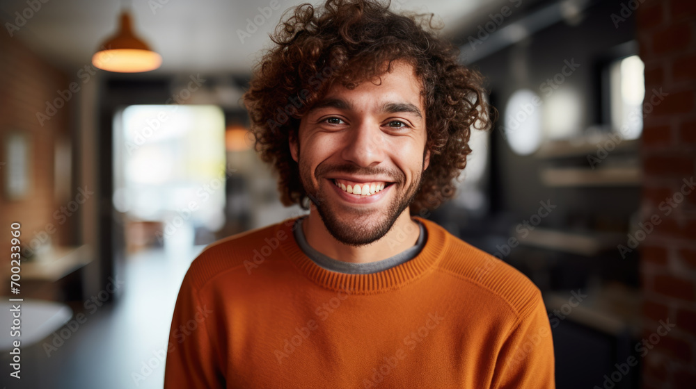 Portrait of a smiling man with curly hair wearing a rust-colored sweater, looking directly at the camera, with a warm and friendly expression Portrait of a smiling man with curly hair wearing a rust-colored sweater, looking directly at the camera, with a warm and friendly expression