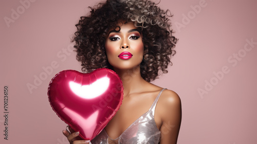 Woman with curly hair smiling while holding a heart-shaped balloon against a pink background. © MP Studio
