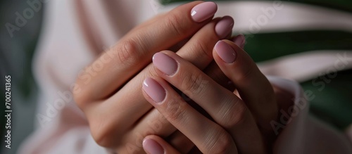 Close-up photo of a woman's hand with a fresh pink manicure applying oil to her cuticles.