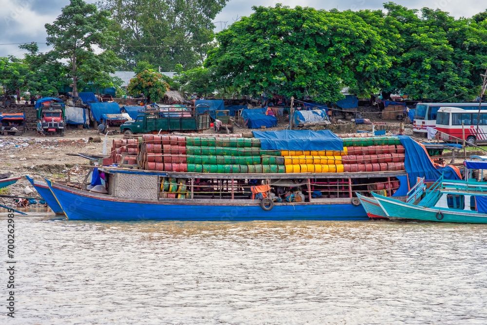 old ships loaded with colored oil barrels and a shore littered with plastic waste 