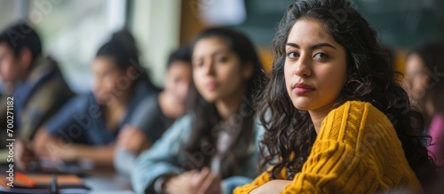 Hispanic female student leads a group of young adults in university classroom.