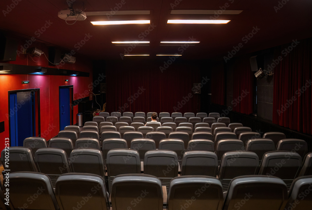 Interior of cinema hall with only one man sitting in the center, closed curtains Interior of cinema hall with only one man sitting in the center, closed curtains