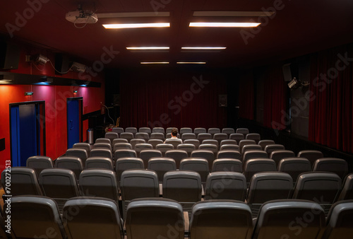Interior of cinema hall with only one man sitting in the center, closed curtains