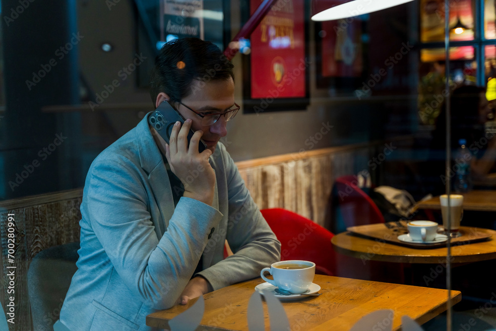 A man in suit talking on a phone sitting inside a cafe with a coffee, business man conversing on phone concept
