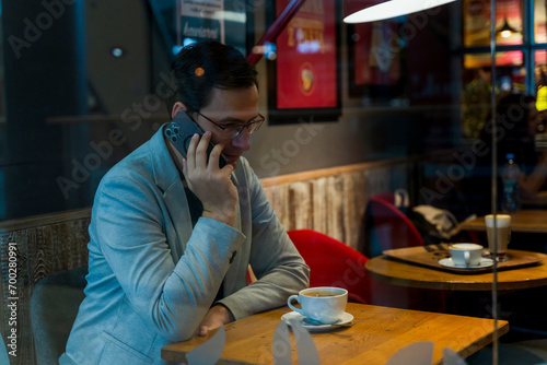 Obraz na płótnie A man in suit talking on a phone sitting inside a cafe with a coffee, business man conversing on phone concept w salonie