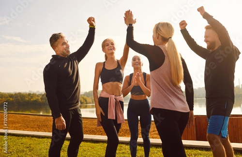 Portrait of group of sport friends standing in the park, exchanging high fives with radiant smiles. The image radiates a sense of community and teamwork during workout as they celebrate together.