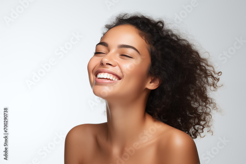 Beautiful laughing young Latin American woman takes care of her skin, posing over grey background