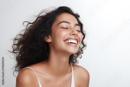 Beautiful laughing young Indian woman takes care of her skin, posing over grey background photo