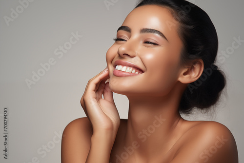 Beautiful laughing young Indian woman takes care of her skin, posing over grey background photo