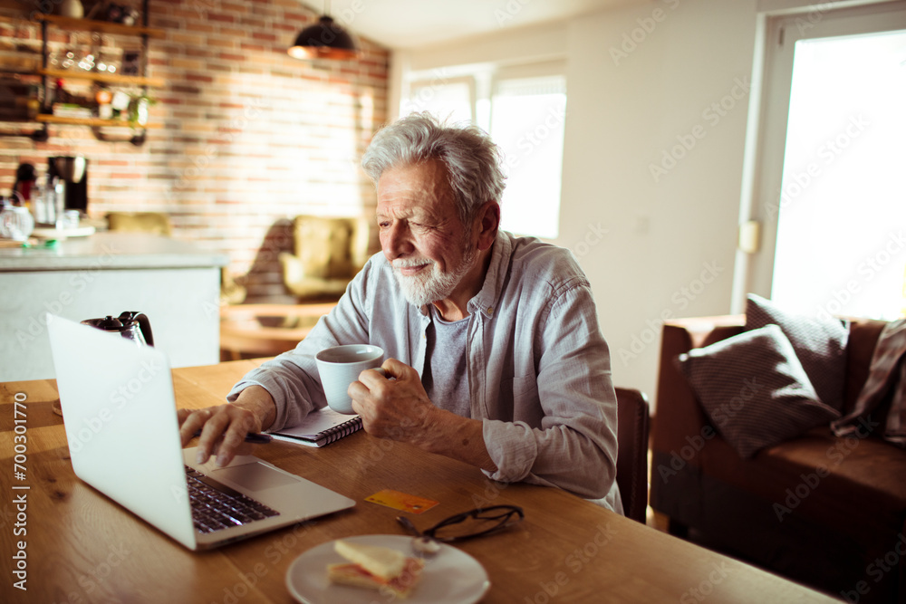 Senior man working at home with laptop and papers on desk Senior man working at home with laptop and papers on desk
