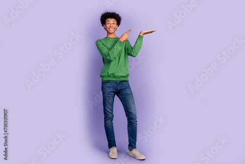 Full length photo of positive excited guy wear green pullover showing finger showing arm empty space isolated purple color background © deagreez