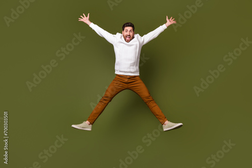 Full length photo of overjoyed glad man dressed white clothes flying air raised hands isolated on khaki color background © deagreez