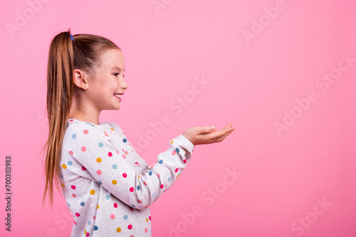 Side profile photo of lovely schoolgirl dressed dotted sleepwear look at offer on palms empty space isolated on pink color background photo