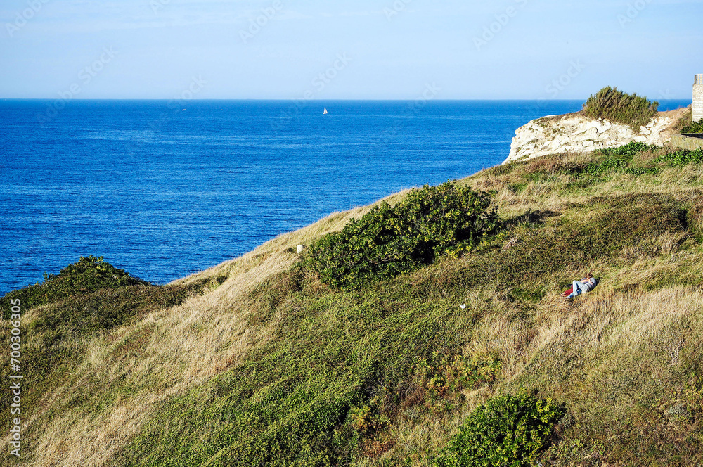 A loving couple lying on the cliff meadow in Sopelana, Spain, facing the sea at sunset. Incredible panorama and two hugging on the hill in summer, shot with a view. A loving couple lying on the cliff meadow in Sopelana, Spain, facing the sea at sunset. Incredible panorama and two hugging on the hill in summer, shot with a view.