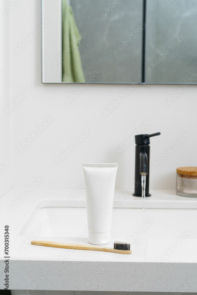 A white mockup of a tube of toothpaste and a wooden toothbrush stand on the sink the background of a stream of water. Vertical image. The concept of natural hygiene products, care for the oral cavity. A white mockup of a tube of toothpaste and a wooden toothbrush stand on the sink the background of a stream of water. Vertical image. The concept of natural hygiene products, care for the oral cavity.