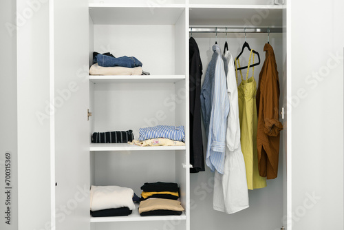Women's wardrobe in the white closet - neatly folded t-shirts and sweaters, dresses on hangers. the concept of compact storage of clothes and organization of space in the room