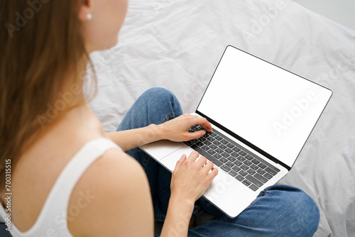 Young woman typing text in laptop with blank mockup screen sitting on sofa. The concept of remote work, solving work tasks and viewing online courses. Background for your advertising text or content.