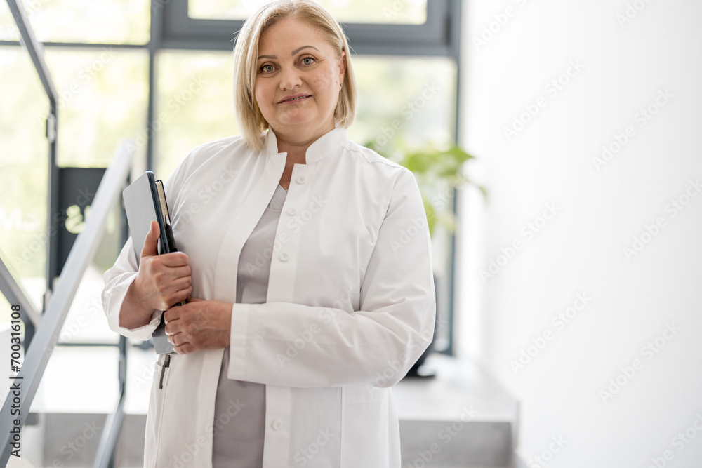Portrait of mid adult nurse in medical gown on staircase at clinic. Beautiful caucasian medical worker with folder indoors Portrait of mid adult nurse in medical gown on staircase at clinic. Beautiful caucasian medical worker with folder indoors